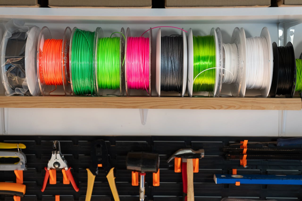 Welkom A variety of colorful filament spools and tools organized on a workshop shelf, ideal for 3D printing enthusiasts.
